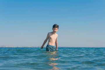 13 years old boy throws up his hands and screaming in the sea waves. Concept of family summer vacation
