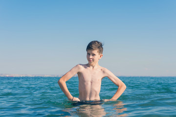 13 years old boy holding hands on hips and outraged standing in the sea waves. Concept