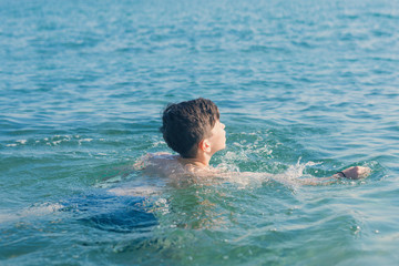 Happy and smiling teen boy swimming in the sea. Travel and summer concept