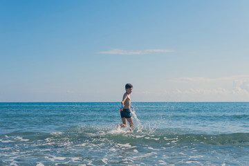 Happy teen boy with snorkeling mask and tube running оn the wave of the sea during summer vacation in the tropical resort town