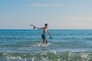 Happy teen boy with snorkeling mask and tube running оn the wave of the sea during summer vacation in the tropical resort town