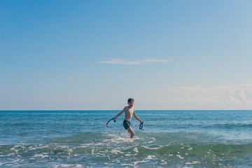 Happy teen boy with snorkeling mask and tube running оn the wave of the sea during summer vacation in the tropical resort town