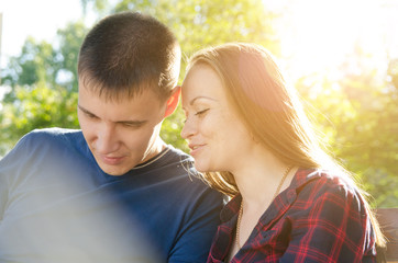 Obraz premium guy in blue T-shirt and girl in plaid shirt are talking while sitting on bench in the park