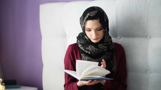 Arabic woman in hijab reading a book in bedroom