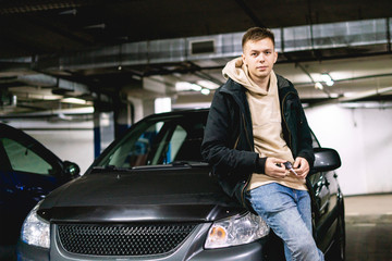 Plakat young man standing with keys of the new car near, on the underground parking f
