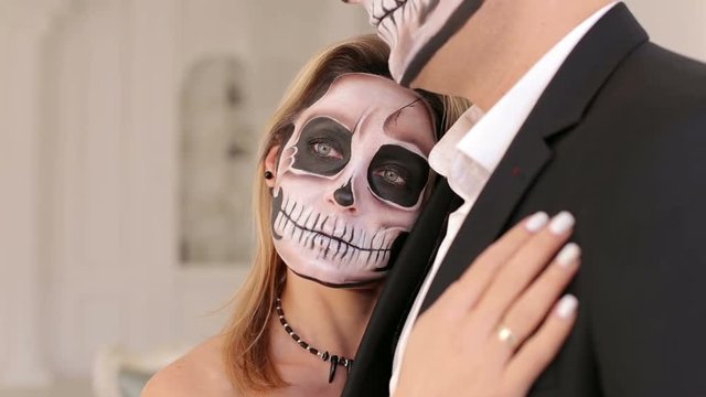 Portrait of a young couple in the Halloween mask. Close-up view of couple of painted halloween holy chracters woman and man. Loving young couple with sugar skull make-up.
