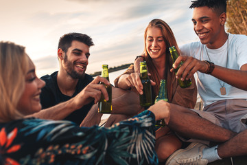 Group of young friends enjoying a day at the lake. They sitting on pier talking, laughing and...