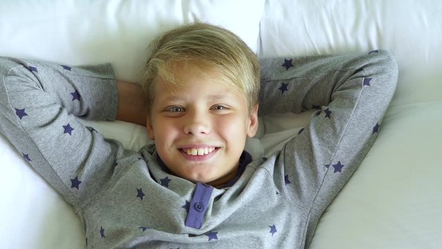 Happy morning concept. Handsome cheerful young boy stretching in bed smiling. Top view real time 4k video footage.