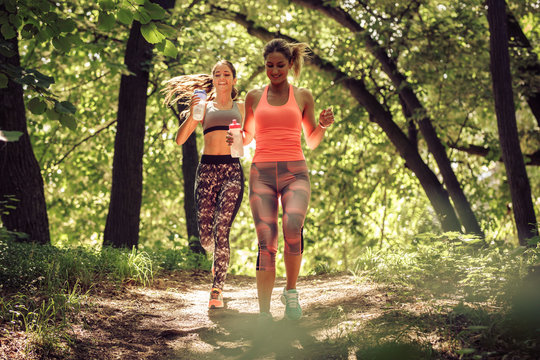 Two young female friends jogging trough the forest.Spring exercise and workout.