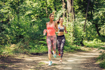 Two young female friends jogging trough the forest.Spring exercise and workout.