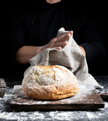 baked round bread on a board behind the cook in black clothes