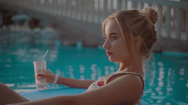 Happy blonde girl drink and relaxing on an inflatable circle look at camera smile cocktail happy holiday pool summer vacation water woman young slow motion
