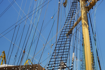 Masts of a sailing ship with the lowered sails with blue sky on the background.
