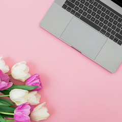 Laptop and bouquet with tulips flowers on pink background. Flat lay. Top view. Computer with tulips.