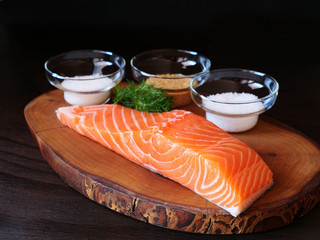 Raw salmon fillet, Salt, sugar in bowls, dill, ingredients for dry cure marinade on dark...