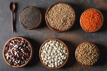 variety of beans, chia seeds and oat groats in bowls with wooden spoon on table