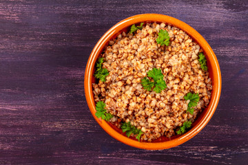 Buckwheat in a rustic earthenware bowl, garnished with fresh parsley leaves, shot from above on a dark wooden background with copy space