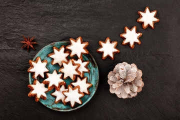 A photo of Zimtsterne, traditional German cinnamon star cookies, shot from the top on a black background with a pine cone and copy space