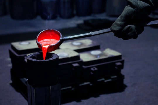 Hand mit Sch&ouml;pfkelle gie&szlig;t fl&uuml;ssiges Metall in Guss Form