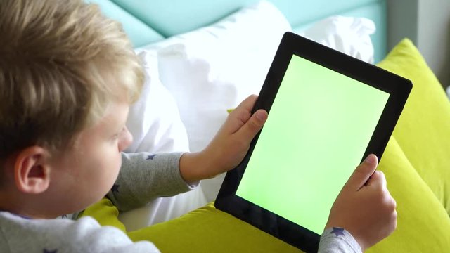 Child holding black tablet pc in hands. Devide with empty blank green screen. Real time 4k video footage.