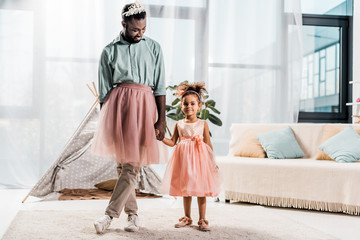 happy african american father and adorable daughter dancing in pink tutu skirts