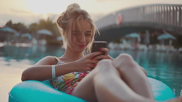 Young blonde girl use phone and relaxing on an inflatable circle happy holiday pool summer vacation water woman young rest close up portrait slow motion