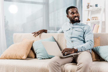 african american freelancer sitting on couch in living room and looking away