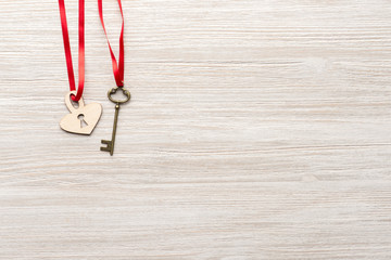 Red ribbon is going through vintage key and a heart lock on wooden background top view. St. Valentine's day. 14 February