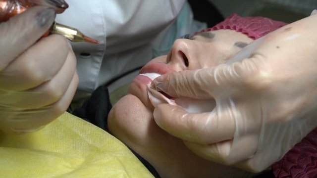 Close-up, the beautician makes a permanent lip makeup woman in a beauty salon and causes her paint needle along the contour of the lip. The view from the top. 4K. 25 fps.