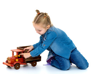 Little girl is playing with a wooden car.