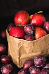 Plums and apples in the craft package on a black background.