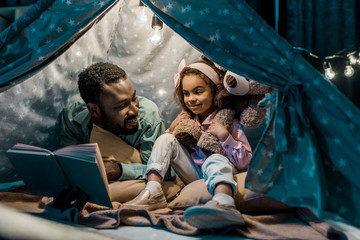 african american dad and daughter sitting in wigwam and reading book © LIGHTFIELD STUDIOS