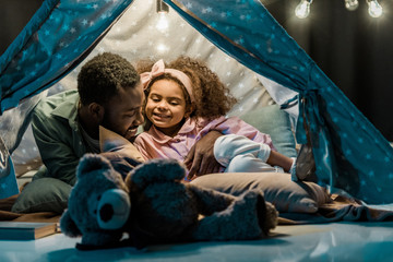 african american dad and daughter lying in wigwam - obrazy, fototapety, plakaty