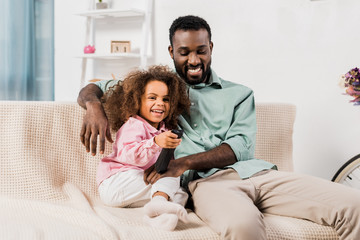 african american dad and daughter watching tv together in living room