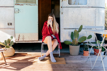 Smiling woman with cup sitting on caravan