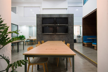 Plasma displays hanging on granite wall in coworking space of modern office. Long wooden table and chairs in center of company room. Corporate business concept