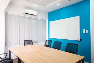 Small conference room with whiteboard on blue wall. Air conditioner above window with blinds. Meeting concept