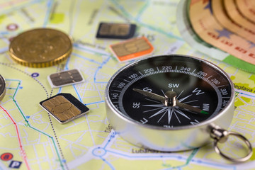 Close-up gsm cards of different sizes lie on the city map surrounded by coins, Euro banknotes and compass