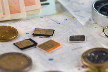Close-up gsm cards of different sizes lie on the city map surrounded by coins, Euro banknotes and compass