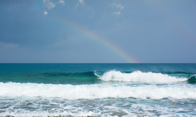 Beautiful view of the raibow over the sea and waves braking on the shore