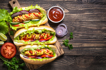 Hot dog with fresh vegetables on wooden table.