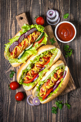 Hot dog with fresh vegetables on dark wooden table.
