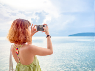 Beautiful asian woman with short hair using smart phone take a photo seascape view