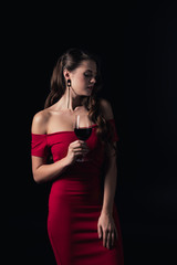 Fototapeta na wymiar attractive woman in red dress holding glass of red wine isolated on black
