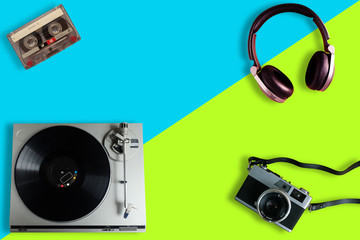 Fototapeta na wymiar Old film camera, Old retro Vinyl record player or turntable, Over-Ear Headphone and cassette tape on a split yellow and blue background, gadgets for The 70-80-90's