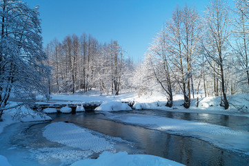 Winter landscape with stream and footbridge in rural terrain