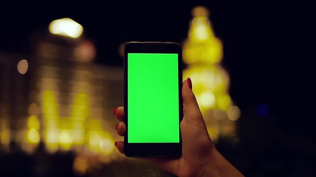 Hand young woman holding phone with vertical green screen blurred city yellow light in night vertical display touchscreen online internet concept communication application
