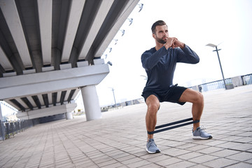 Young sporty man doing exercises with rubber band outdoor.