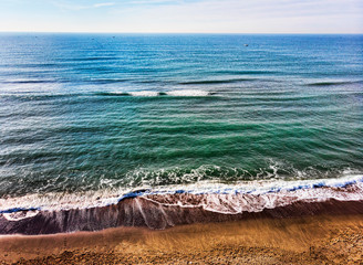 Top view of the beach and a blue and calm ocean with many boats in the distance