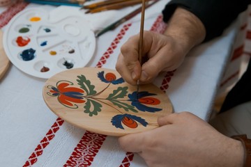 handpainting on handmade decorative wooden round plate, man's hand paints a bright floral pattern...
